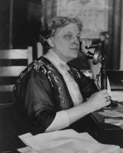 Black and white photo of Carrie Chapman Catt speaking on an old fashioned candlestick phone. LOC Carrie Chapman Catt. Collections of the Library of Congress.